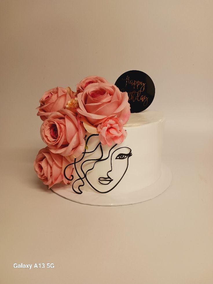 a white cake decorated with pink roses and a black happy birthday sign on top that says happy birthday