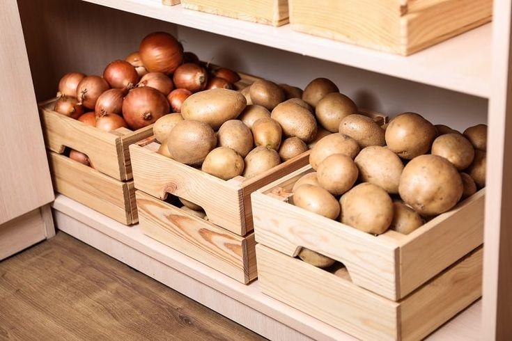 potatoes and onions are in wooden boxes on the shelf