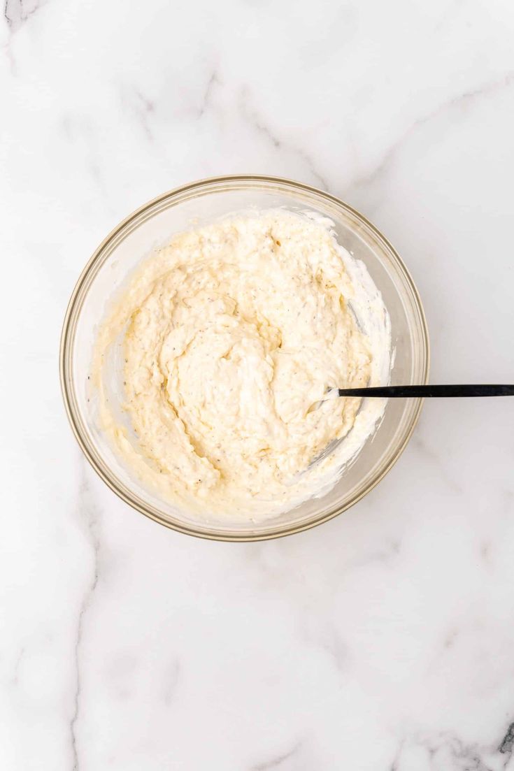 a glass bowl filled with cream on top of a white countertop next to a black spoon