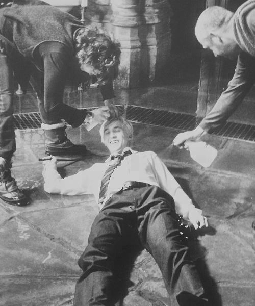 two men and a woman standing over a man laying on the ground