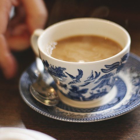 a cup of coffee sitting on top of a saucer next to a person's hand