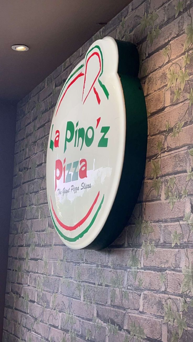 a pizza sign mounted to the side of a brick wall next to a green and white clock