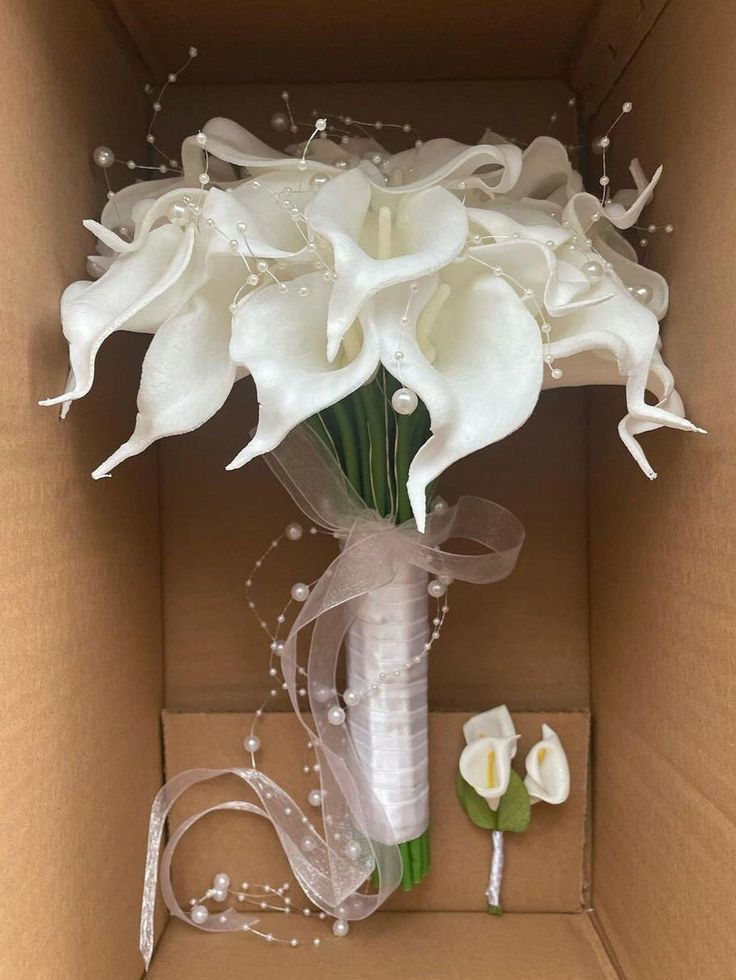 a bouquet of white flowers in a cardboard box with ribbons and pearls on the side