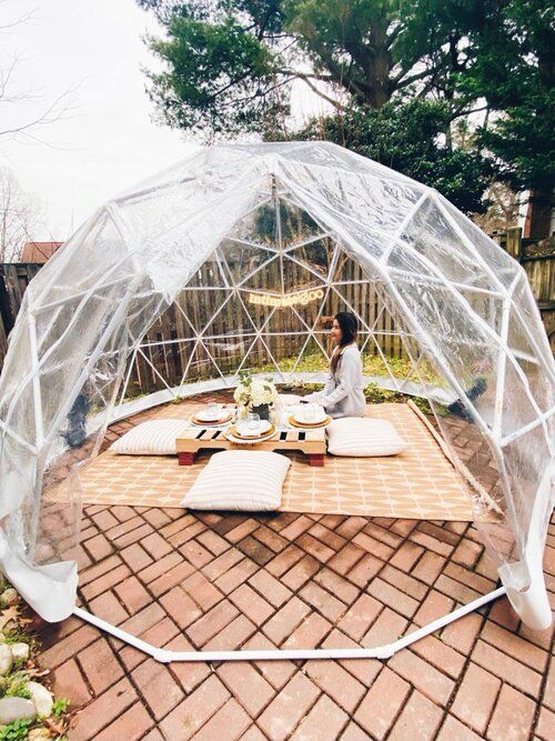 a woman sitting at a picnic table in a clear plastic dome with food on it