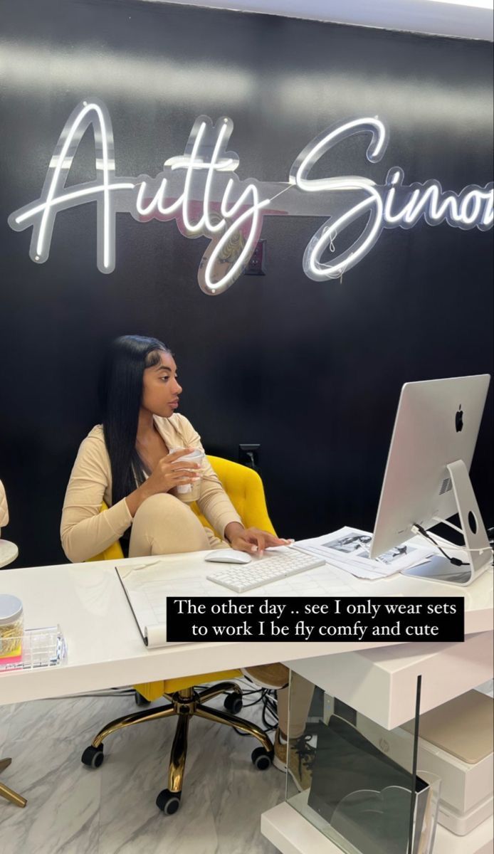 a woman sitting in front of a laptop computer on top of a white desk next to a yellow chair