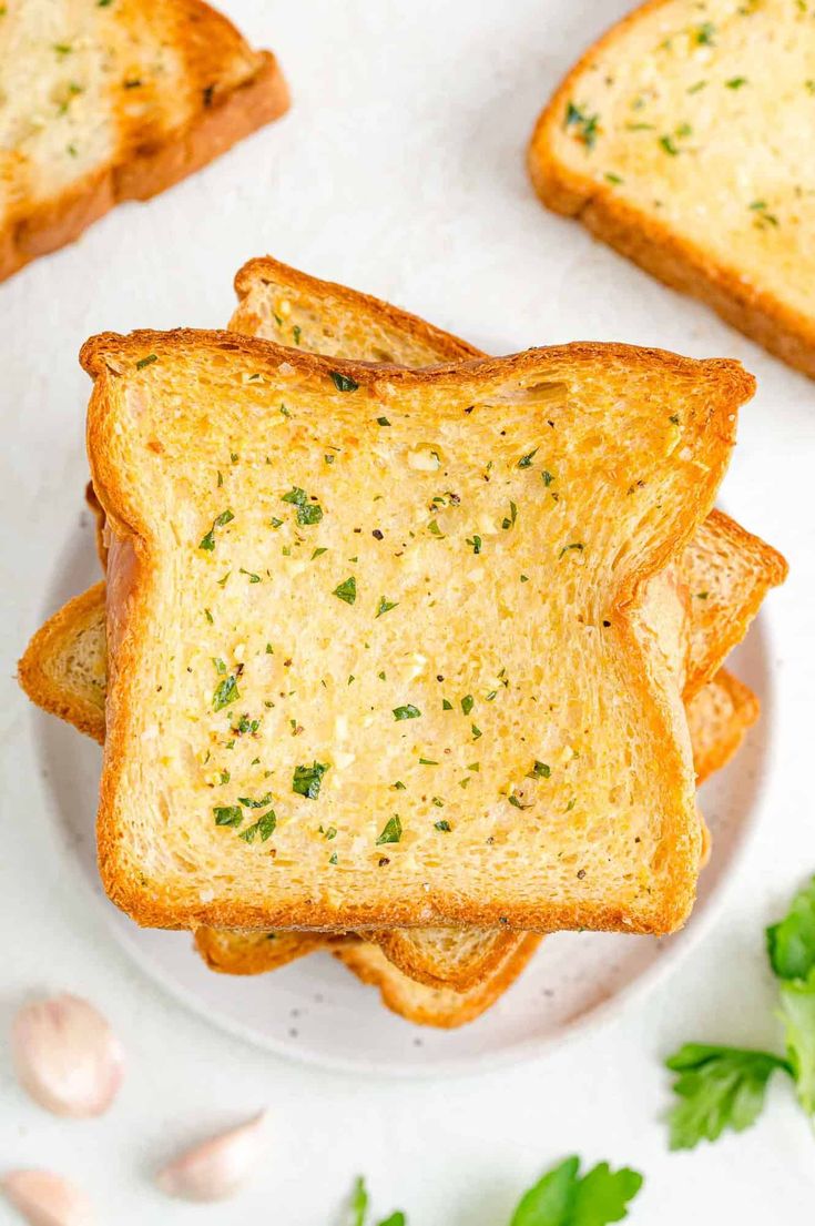 four slices of garlic bread on a white plate with parsley and garlic flakes