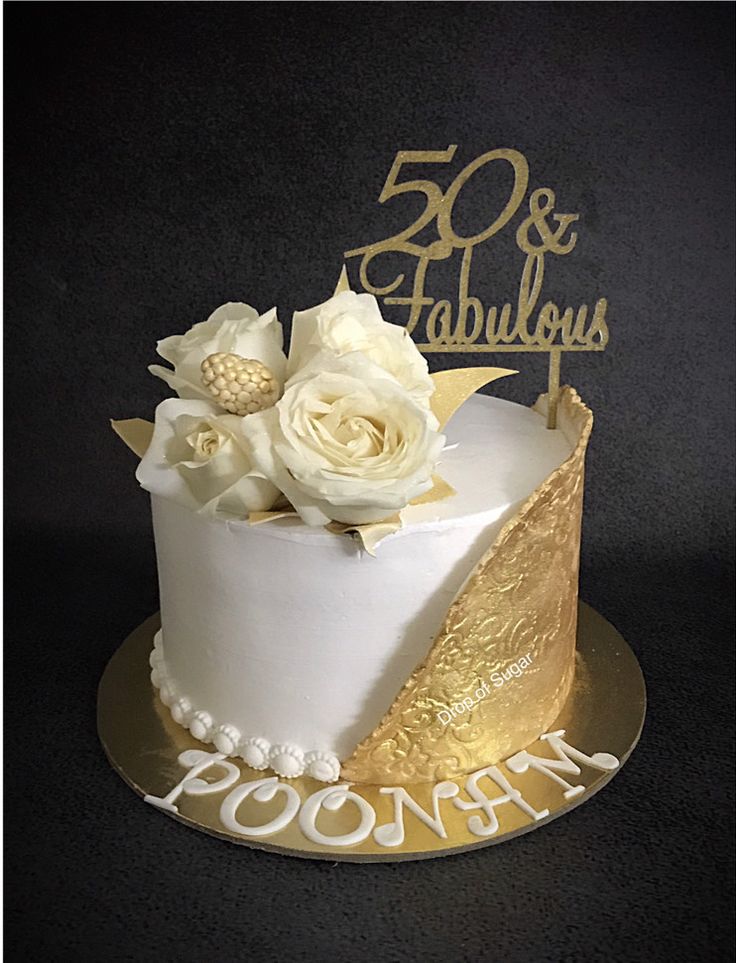 a white and gold 50th birthday cake with flowers on the top is sitting on a black surface