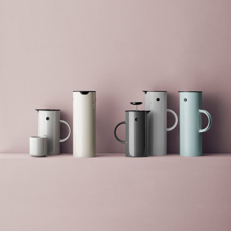 four different colored coffee mugs lined up against a pink wall, one is white and the other is grey