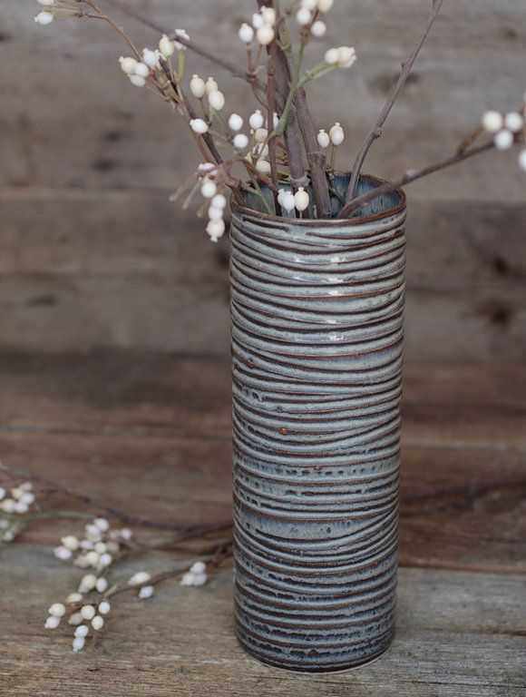 a metal vase with flowers in it sitting on a wooden table next to some branches