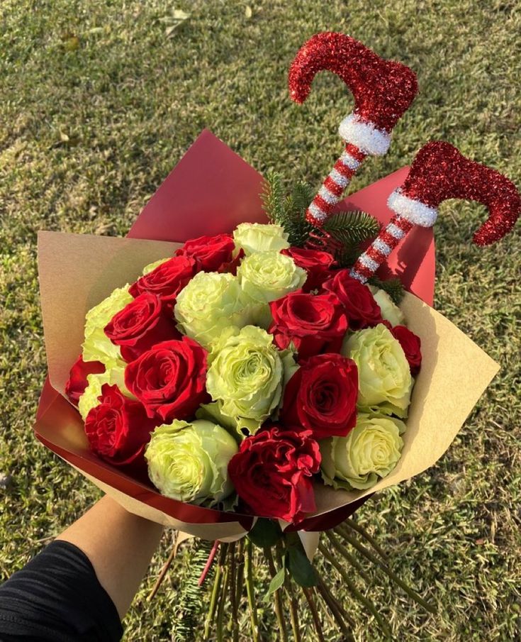 someone is holding a bouquet with roses and candy canes on the grass in front of them