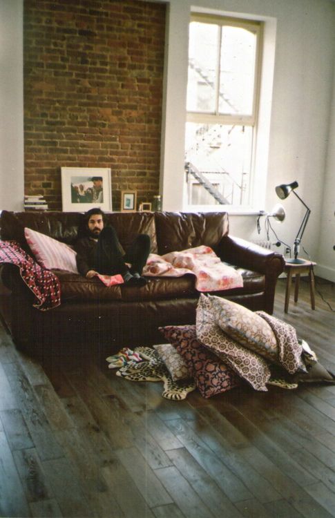 a man sitting on top of a brown couch in a living room next to a window