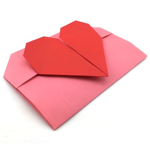 an origami heart on top of a pink envelope with red paper folded over it