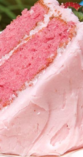 a piece of cake with pink frosting on a plate next to some strawberries