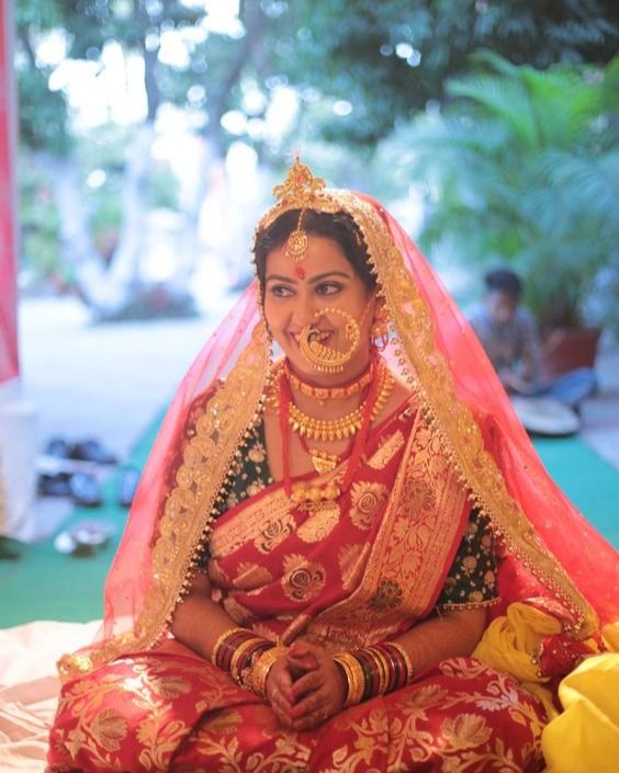 a woman sitting on top of a bed wearing a red and gold wedding outfit with jewelry