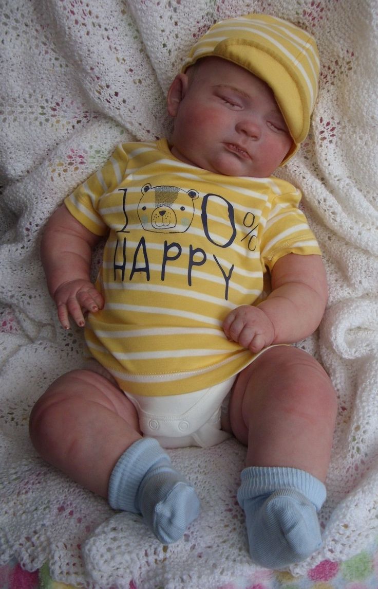 a baby laying on top of a blanket wearing a yellow and white shirt with the words happy written on it