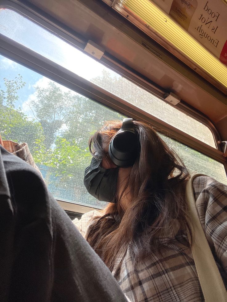 a woman wearing a mask and looking out the window on a bus with trees in the background