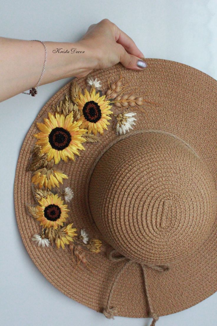 a woman's hand holding onto a straw hat with sunflowers on it