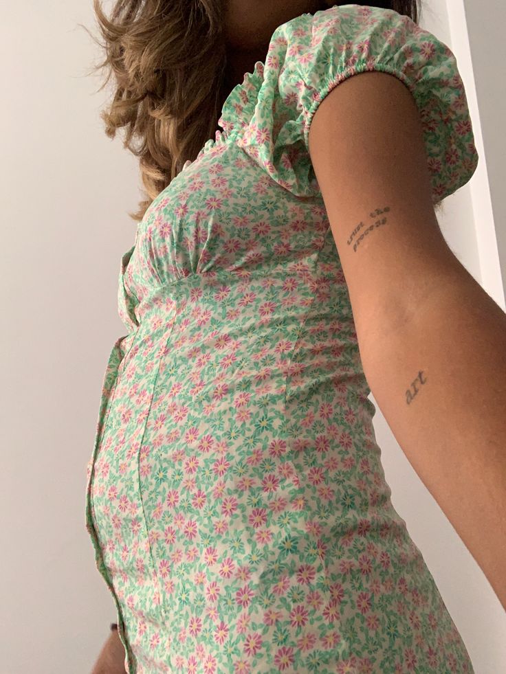 a pregnant woman wearing a floral dress and holding her hand on the back of her stomach