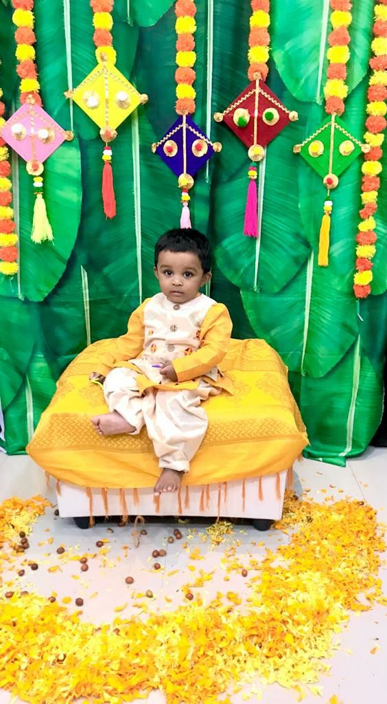 a little boy sitting on top of a bed in front of a green backdrop with yellow flowers