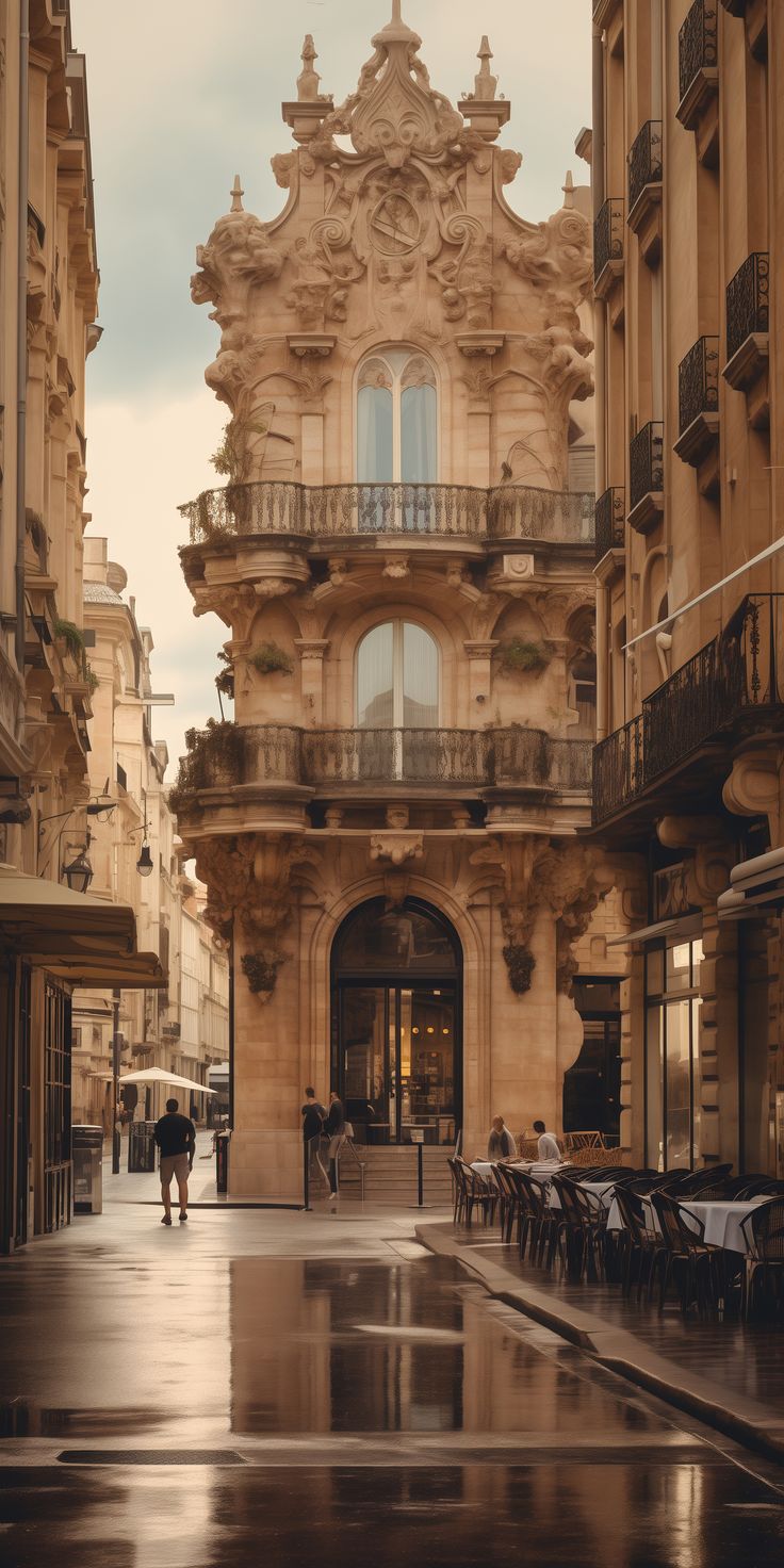 an empty street with tables and chairs in front of a building on a rainy day