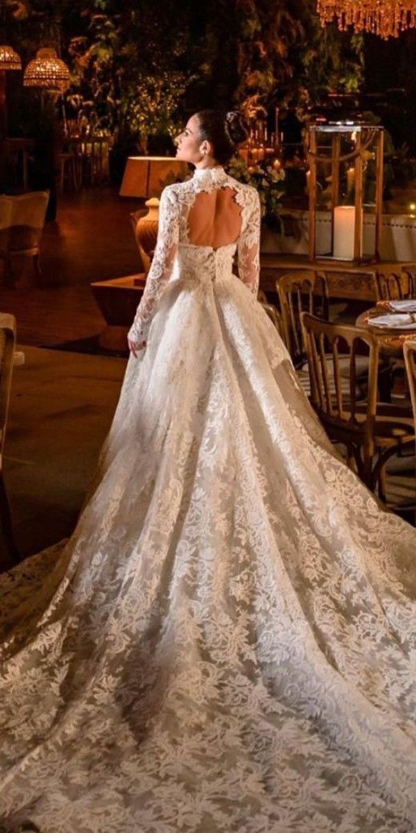 a woman in a wedding dress looking at the back of her gown with long sleeves