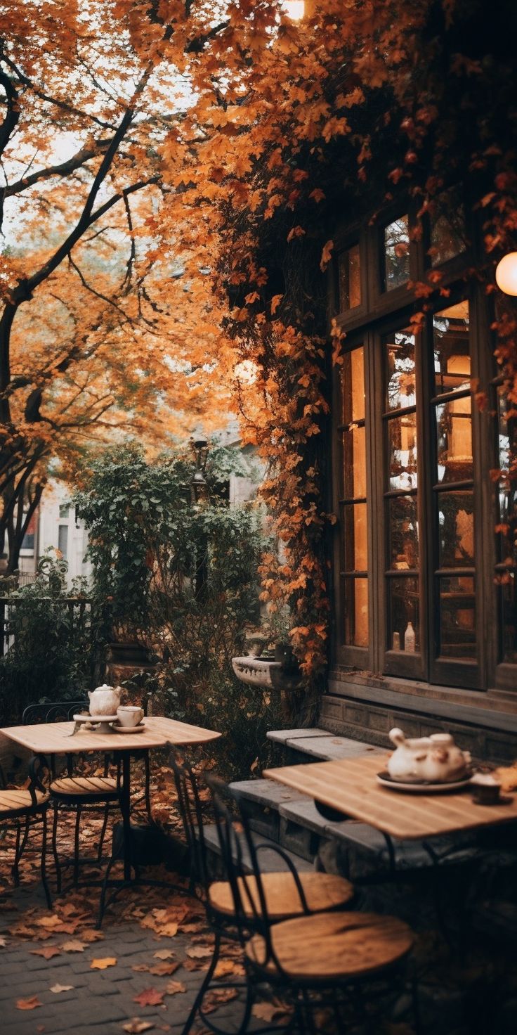 an outdoor cafe with autumn leaves on the ground and tables set up for two people