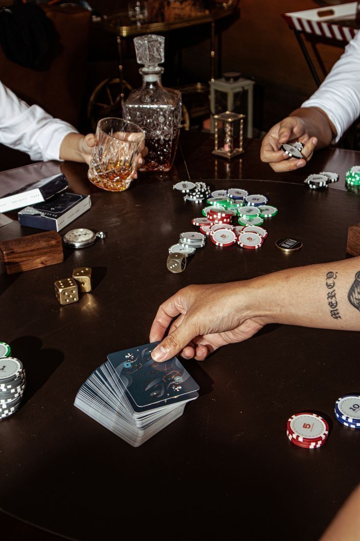 two men playing cards at a table with other people sitting around the table and holding their hands together