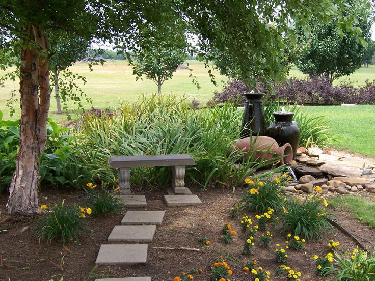 a stone bench sitting in the middle of a garden with yellow flowers and trees around it