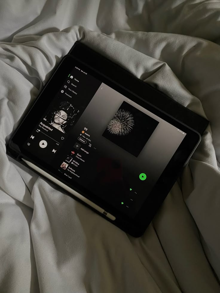 a tablet sitting on top of a bed covered in white sheets and pillows, with an image of fireworks coming out of the screen