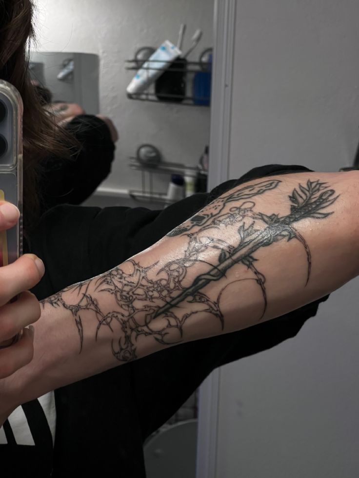 a woman taking a selfie with her cell phone in front of her arm tattoo