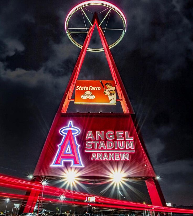 an angel stadium sign lit up at night with lights on the building and cars passing by