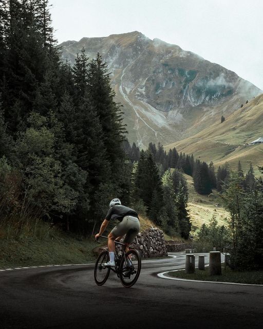 a man riding a bike down a curvy road in front of a mountain