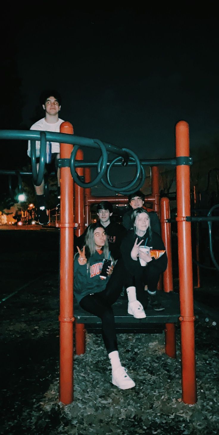 three people sitting on top of a playground structure at night with their arms around each other