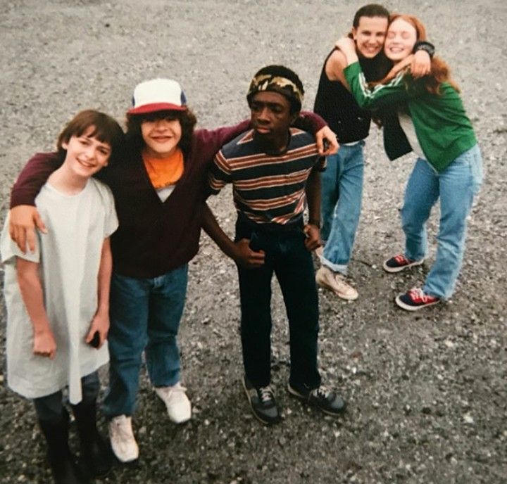 a group of young people standing next to each other on top of a dirt field