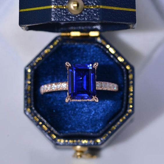 an engagement ring with a blue stone surrounded by white and yellow diamonds in a velvet box