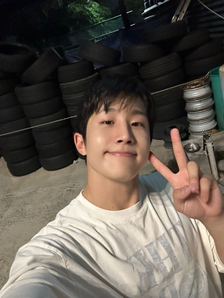 a young man is making the peace sign with his fingers in front of stacks of tires