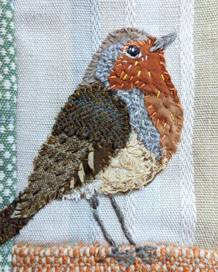 a small bird is sitting on the edge of a piece of fabric with stitching