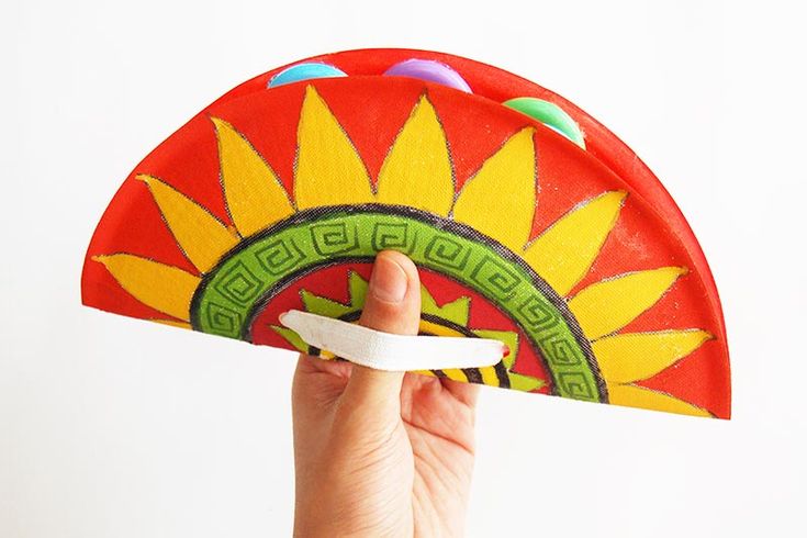 a hand holding a red and yellow fan with green designs on the front, against a white background