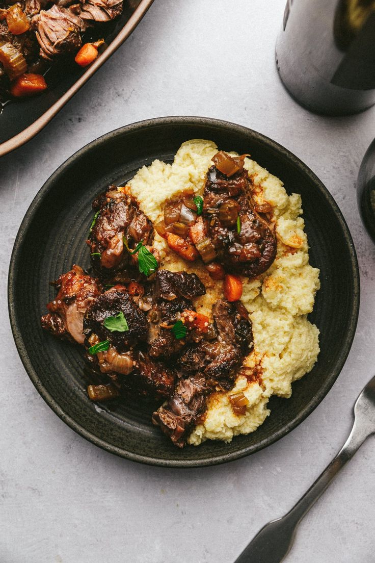 a black plate topped with meat and mashed potatoes