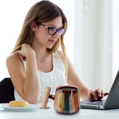 a woman sitting at a table with a laptop computer in front of her and looking at the screen