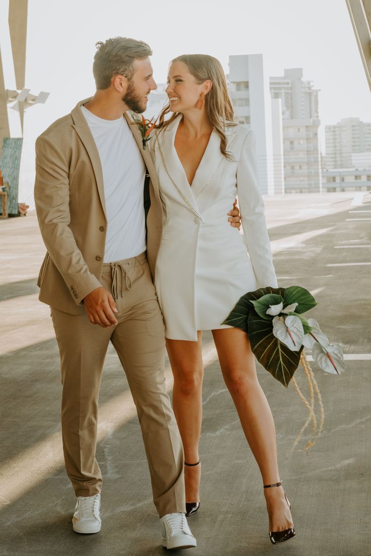 a man and woman standing next to each other in front of a building holding flowers