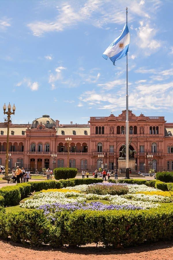 a large building with a flag flying in front of it's entrance and flower garden