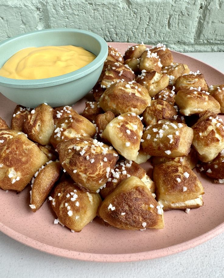 a pink plate topped with pastries next to a bowl of mustard and dipping sauce