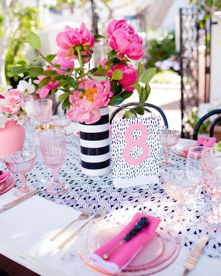 the table is set with pink flowers and black and white striped vases on it