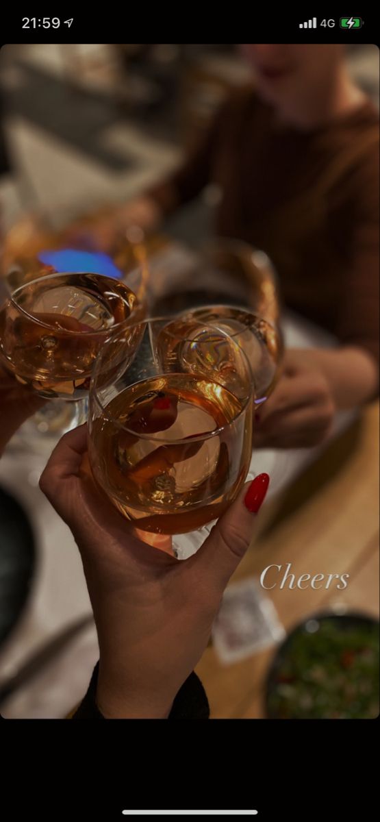 two people holding wine glasses in their hands with the words cheers on them and one person sitting at a table