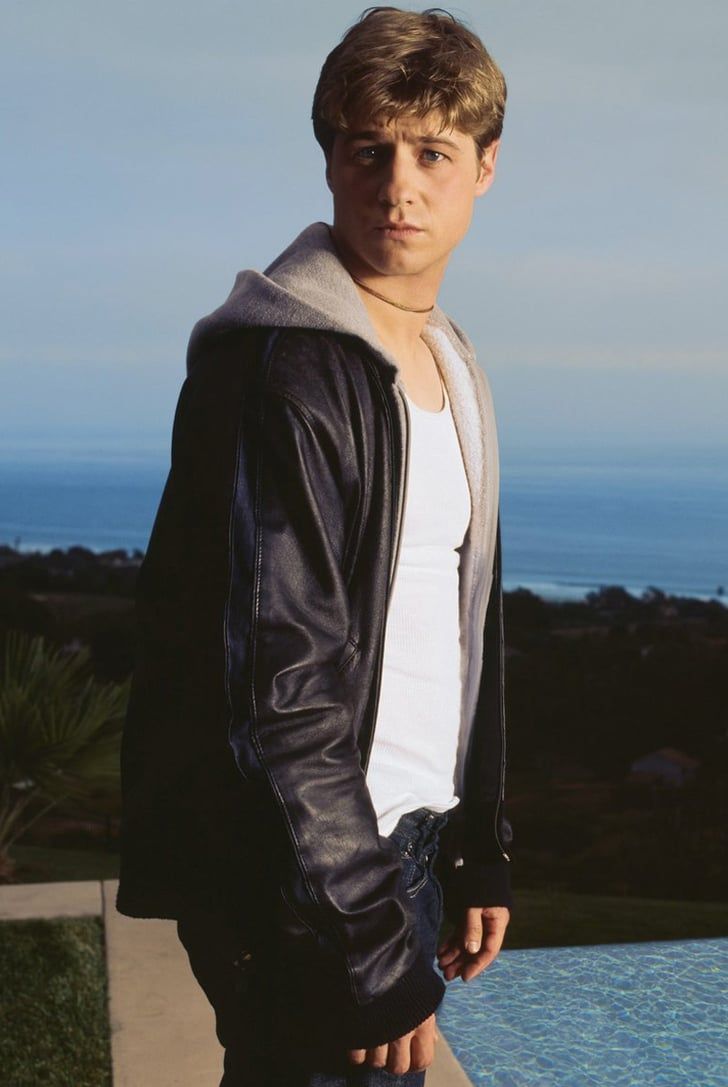 a young man standing in front of a swimming pool wearing a black jacket and white t - shirt