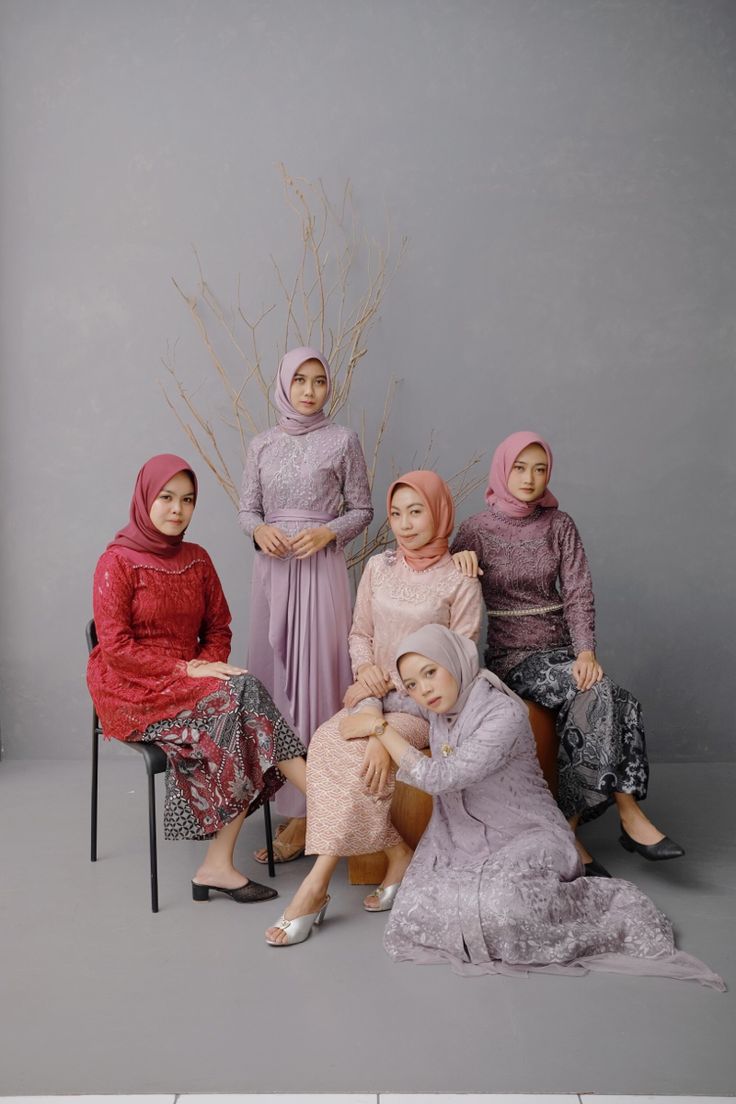 four women sitting next to each other in front of a gray wall and one is holding a baby