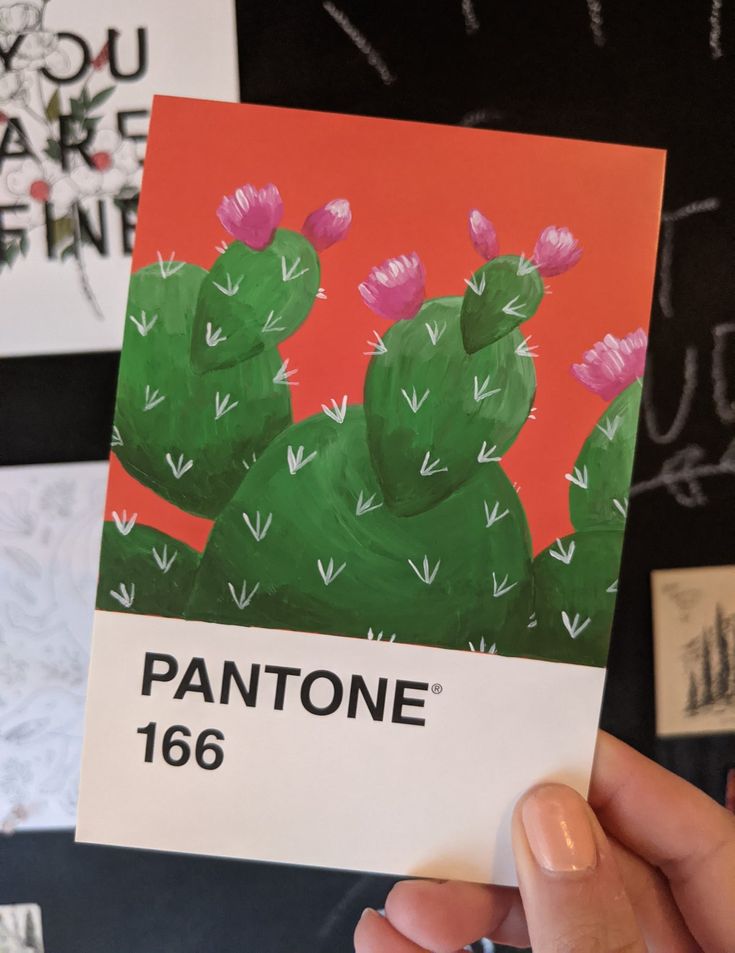 a person holding up a card with a painting of a cactus on it and the words pantone in front of them