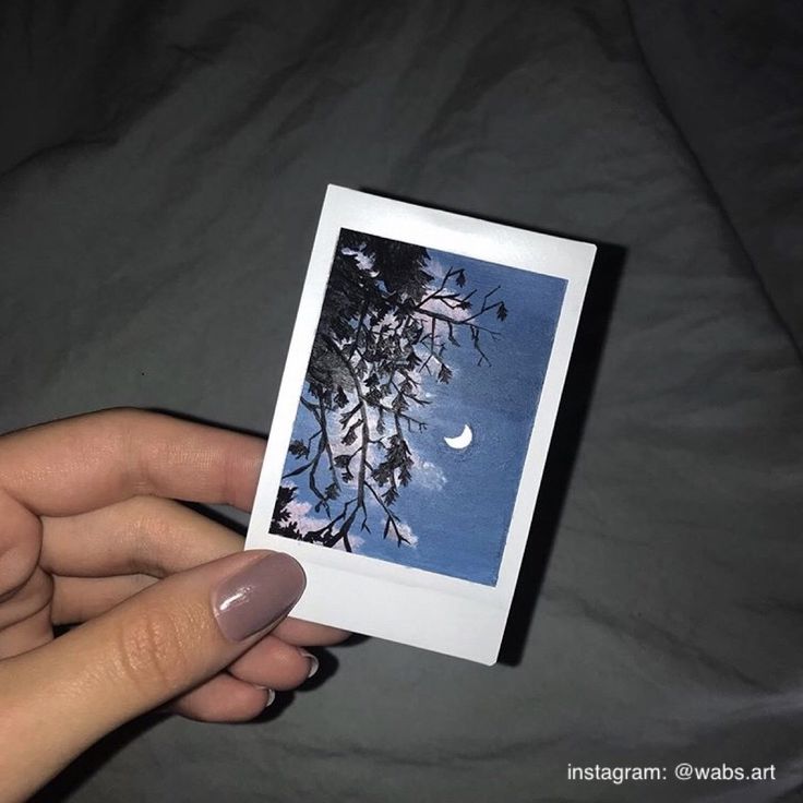 a person holding up a polaroid with the moon in the sky behind them on a bed