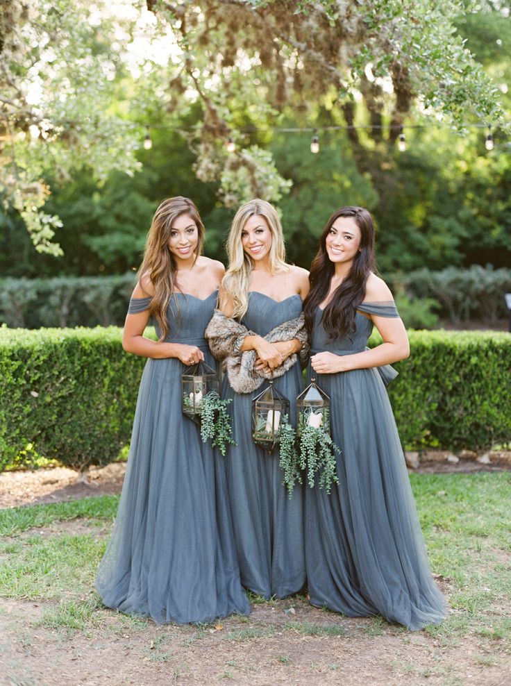 three bridesmaids pose for a photo in front of some bushes and trees with their bouquets